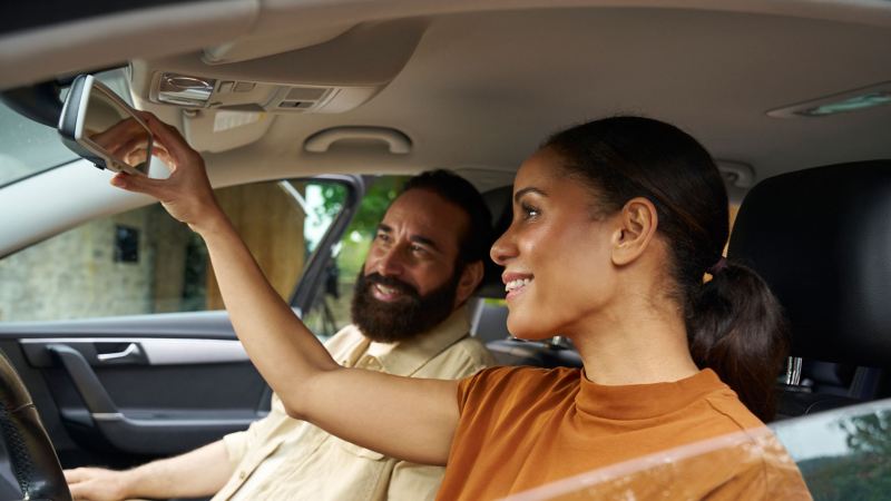 Couple sitting in a VW mid-size class Passat, she adjusts the interior mirror