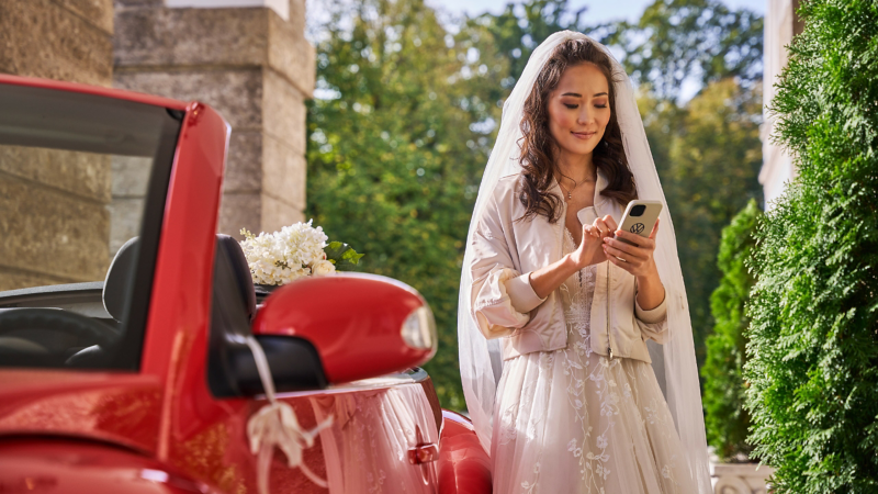 Une mariée à côté d’une VW New Beetle regarde son smartphone