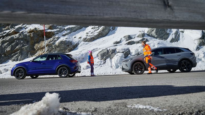 Ein VW Servicemitarbeiter geht auf eine Kundin und ihr VW Auto in verschneiter Landschaft zu