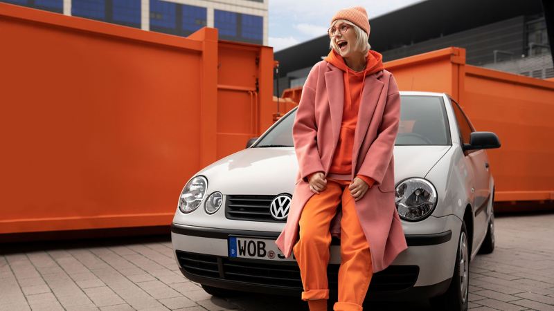 Eine Frau lehnt sich an ihren gebrauchten Kleinwagen von Volkswagen