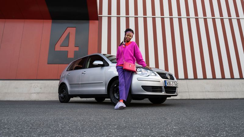 Eine Frau lehnt sich an ihren gebrauchten Kleinwagen von Volkswagen
