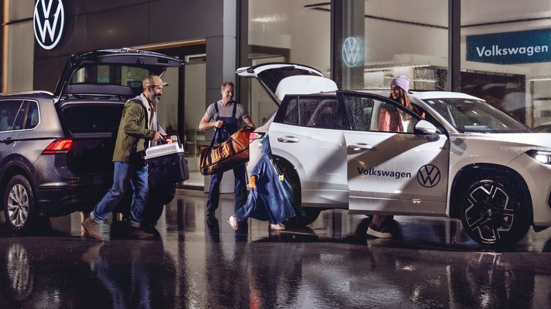 VW Servicemitarbeiter hilft Kunden beim Tragen von Gegenständen von einem VW Auto in ein anderes
