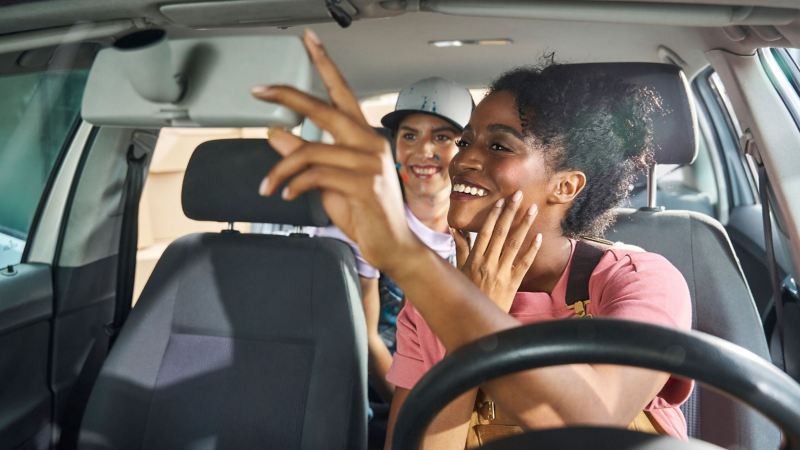 Woman looks through the interior mirror at her friend in the back seat