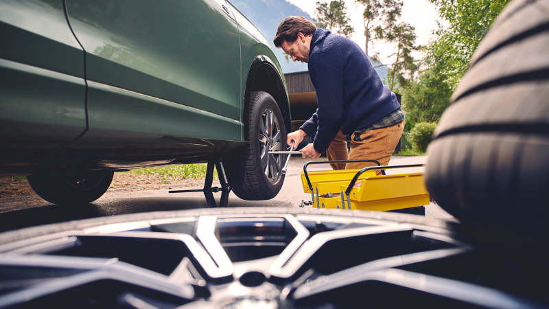 Mann beim Räderwechsel an einem VW Tiguan, im Vordergrund zwei VW Räder, die aufeinander liegen