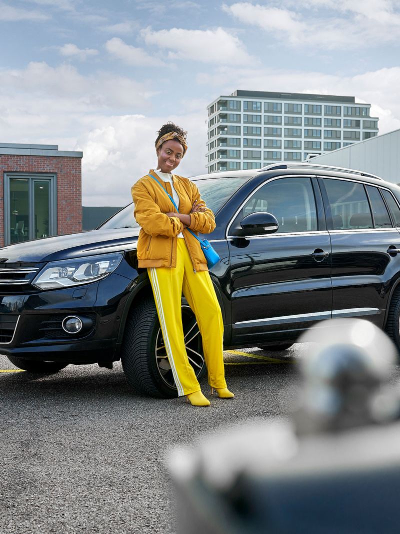 Eine Frau in gelber Kleidung lehnt an ihrem VW Tiguan 1