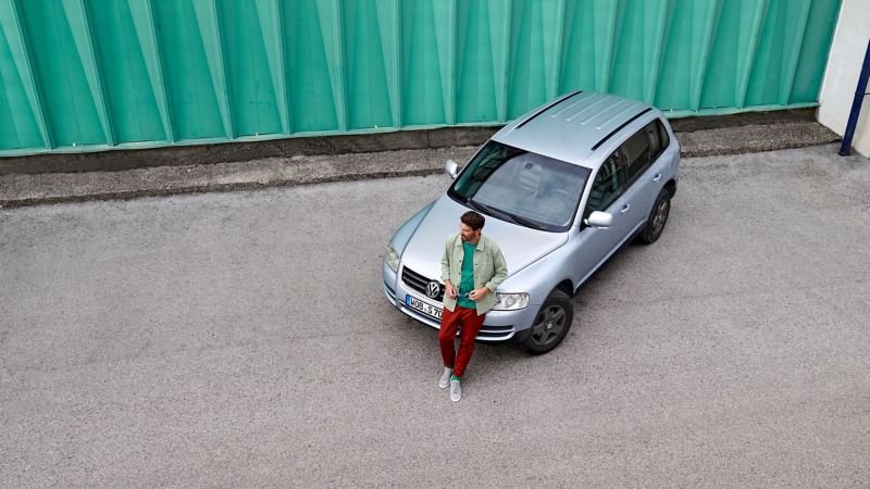 Vogelperspektive von Mann vor grüner Wand, der sich an silbernen VW Touareg 1 lehnt