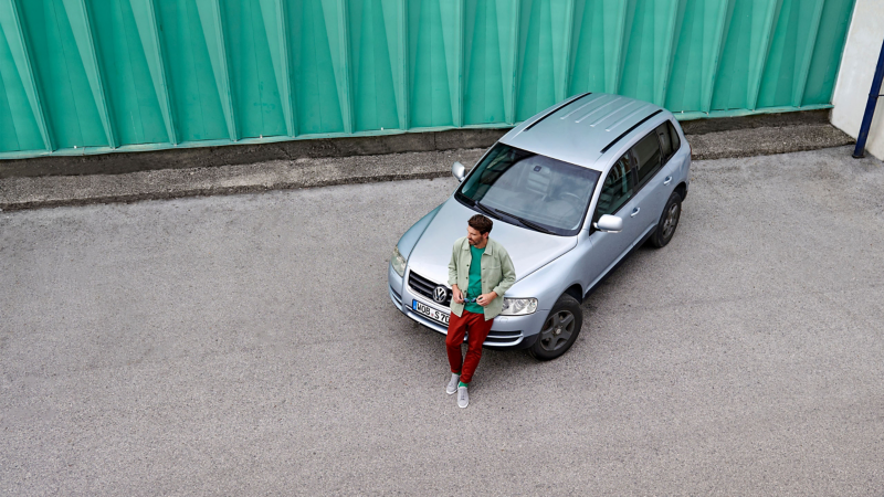 Bird's eye view of man in front of a green wall leaning against silver VW Touareg 1