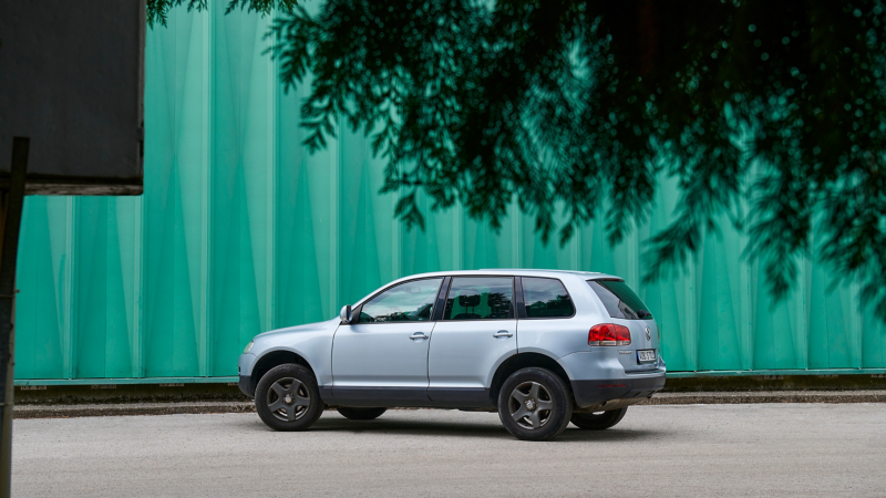 VW Touareg 1 stands in front of a green wall with a branch and sign in the foreground