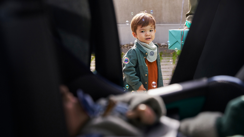 View through open car door shows child surrounded by soap bubbles