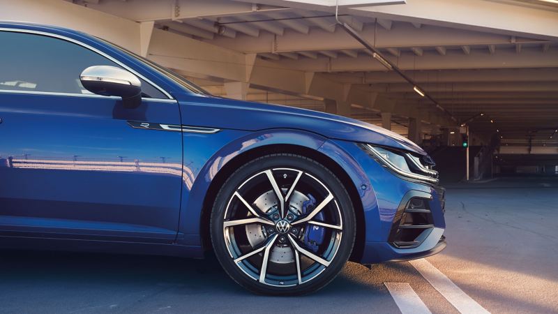 Niebieski Volkswagen Arteon R Shooting Brake stoi na placu przed wielopoziomowym parkingiem.