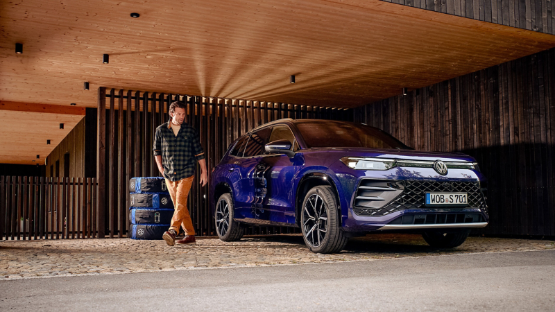 Uomo che si allontana da un VW Tayron, accanto quattro ruote impilate riposte in sacche copripneumatici Volkswagen Accessori.