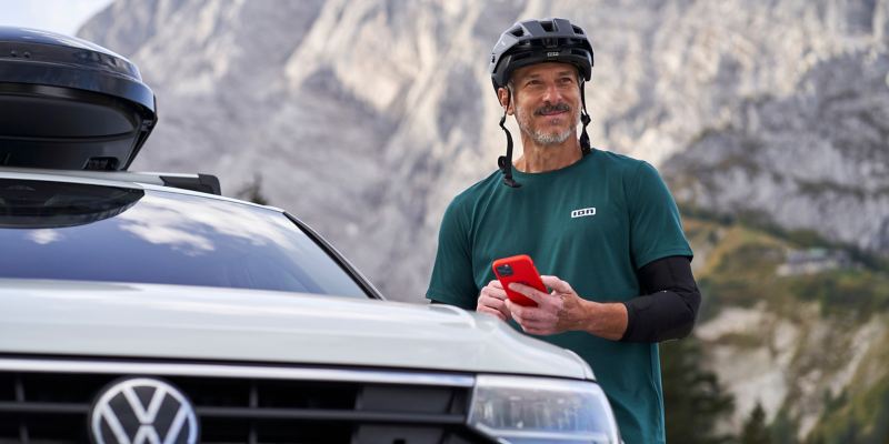 Man with helmet next to VW Tiguan 2 holds smartphone in his hand