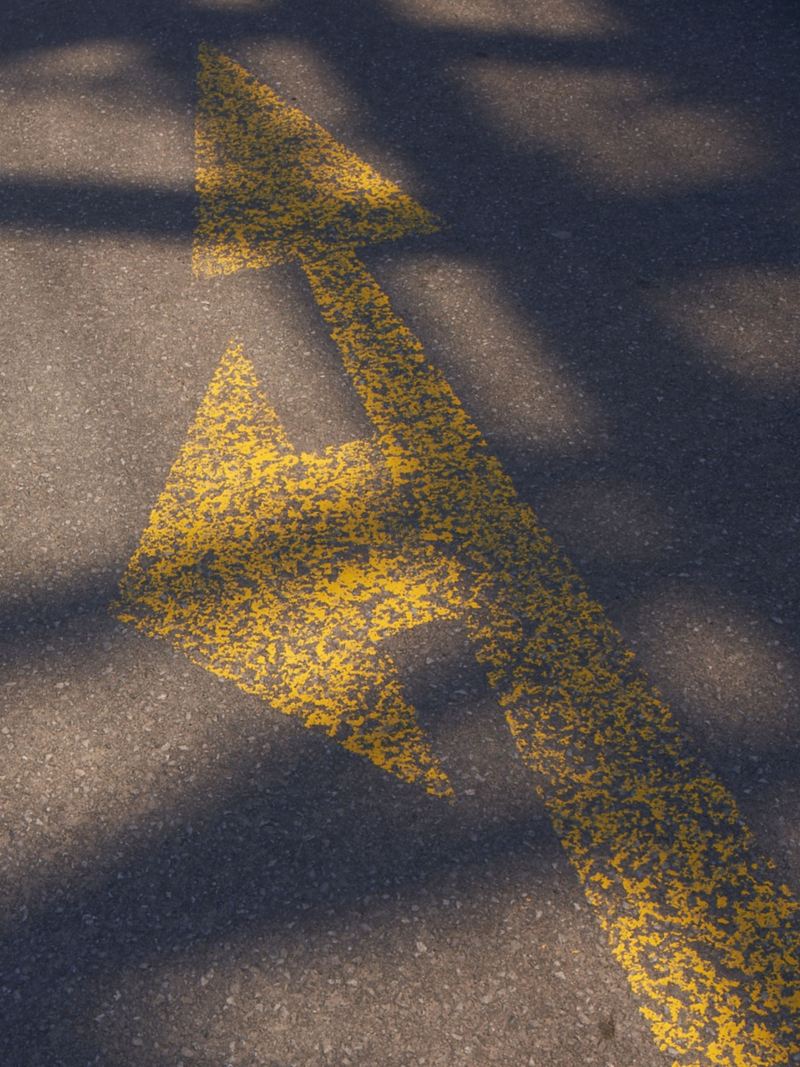 A double arrow on asphalt, one pointing left, the other straight ahead