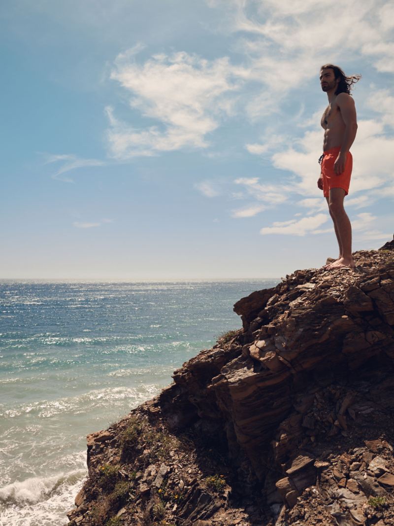 Een man staat op een rots en kijkt uit over de zee