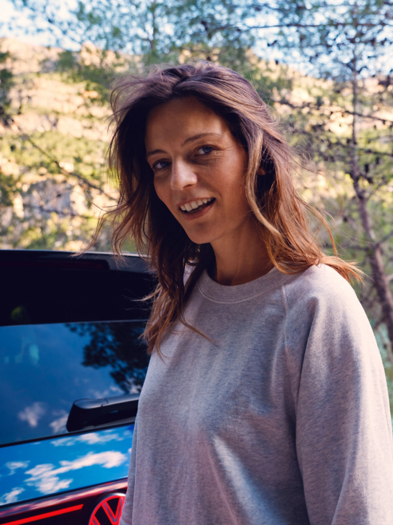 Une femme se tient devant le coffre d’un VW Touareg R et regarde la caméra