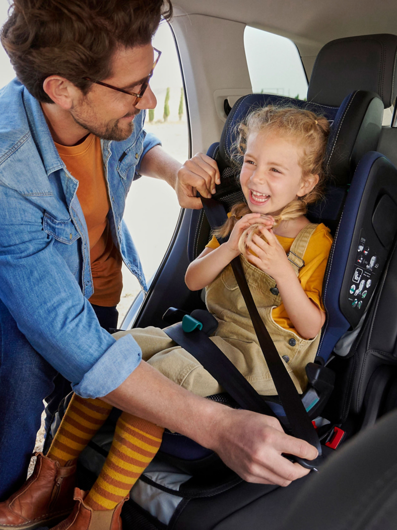 Mann schnallt Kind an, das in einem VW Kindersitz sitzt