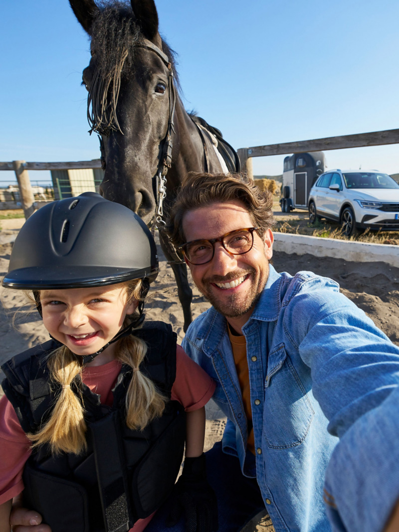 Ojciec, córka i koń na selfie, VW Tiguan z przyczepą konną w tle