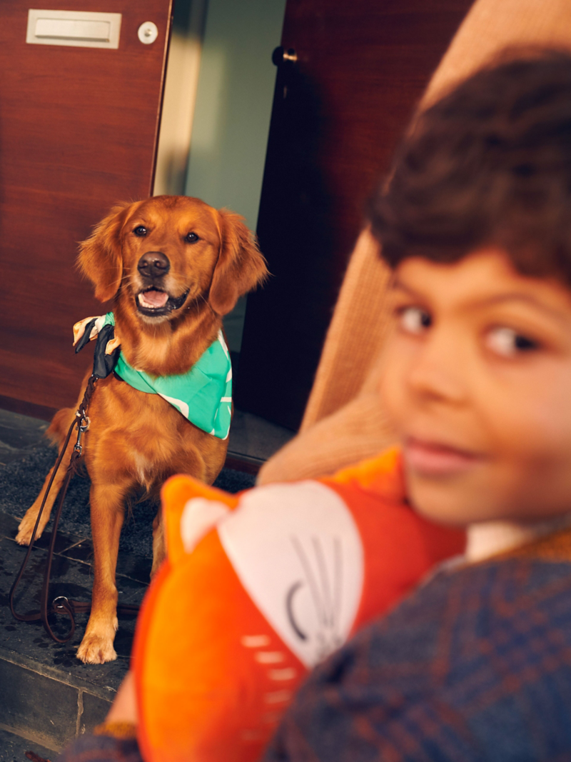 Et barn smiler til kameraet, i baggrunden sidder der en hund