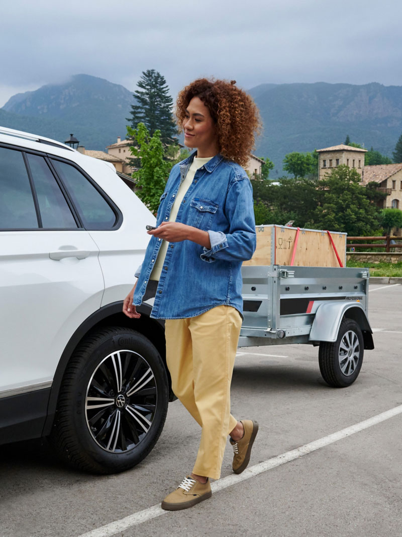 Woman standing next to a VW car towing loaded low-loader