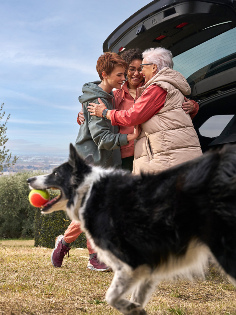 Happy family with dog in front of open luggage compartment of VW Touareg