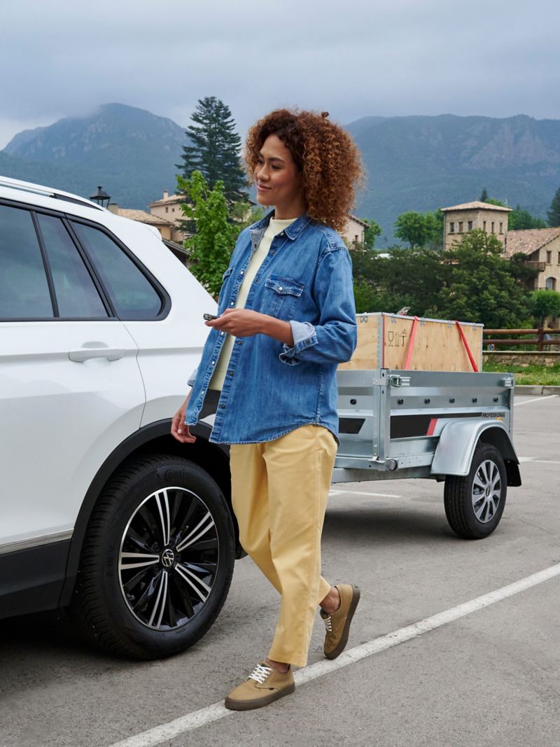 Frau steht neben VW Auto, das beladenen Tieflader zieht