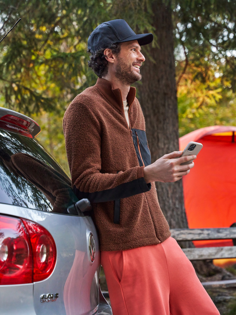 Homme avec un smartphone à la main appuyé contre une VW Golf 5