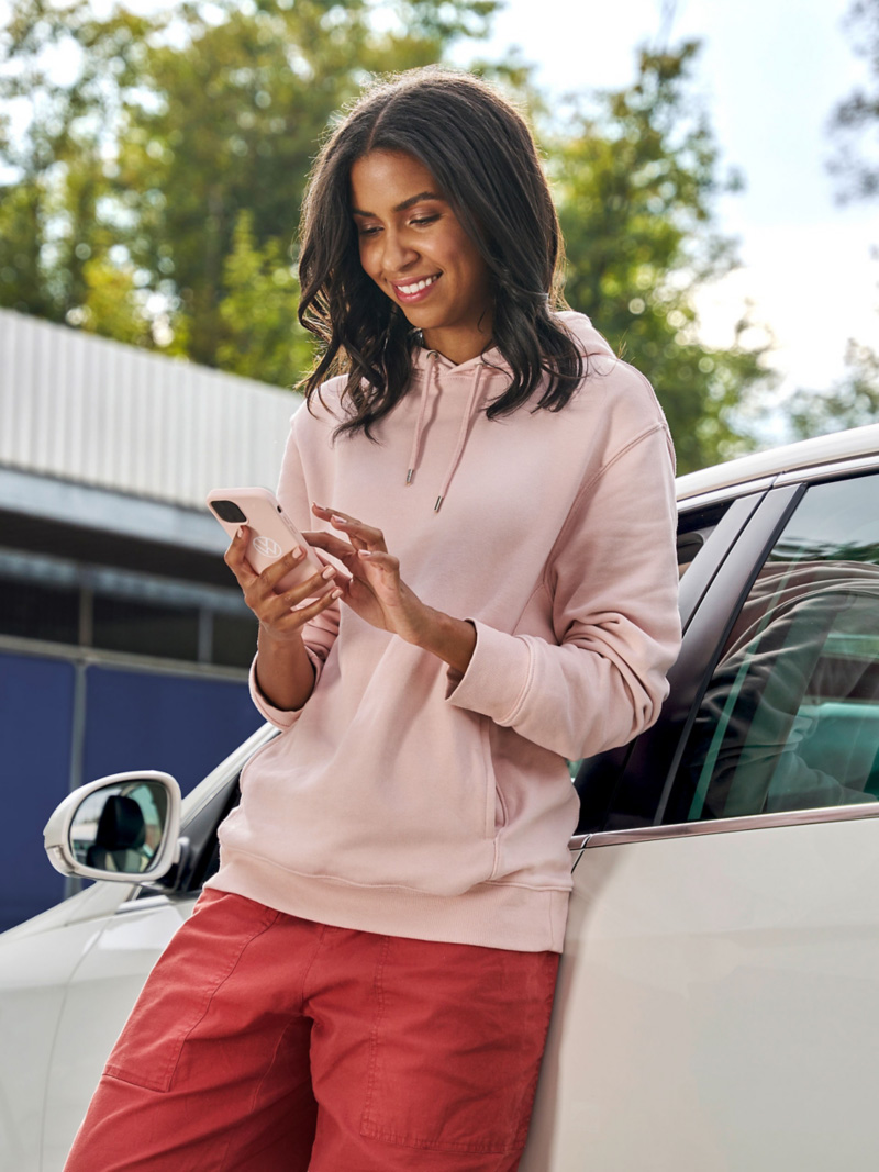 Kobieta opiera się o VW Passat B6 i patrzy na smartfon