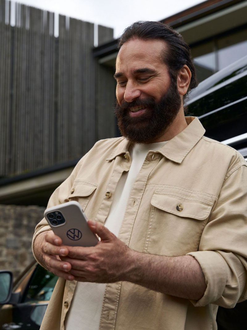 Man leaning against a VW Passat B7 and looking at his smartphone