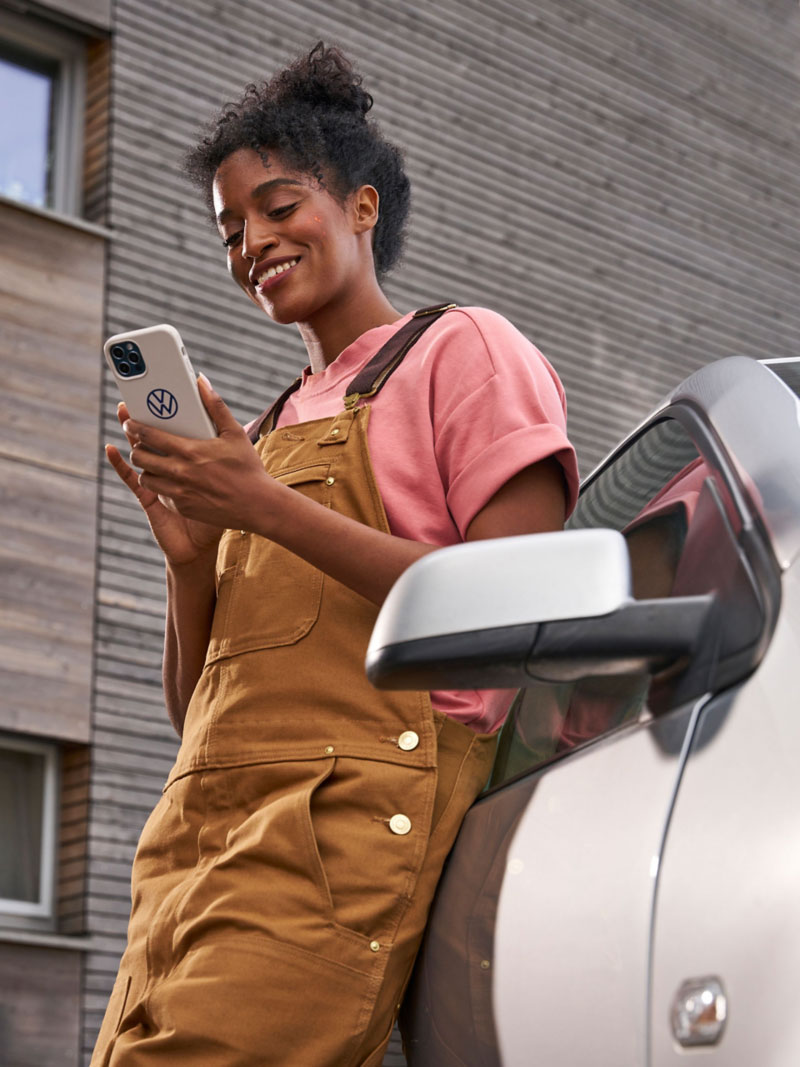 Woman leaning against a VW Polo 4 and looking at her smartphone