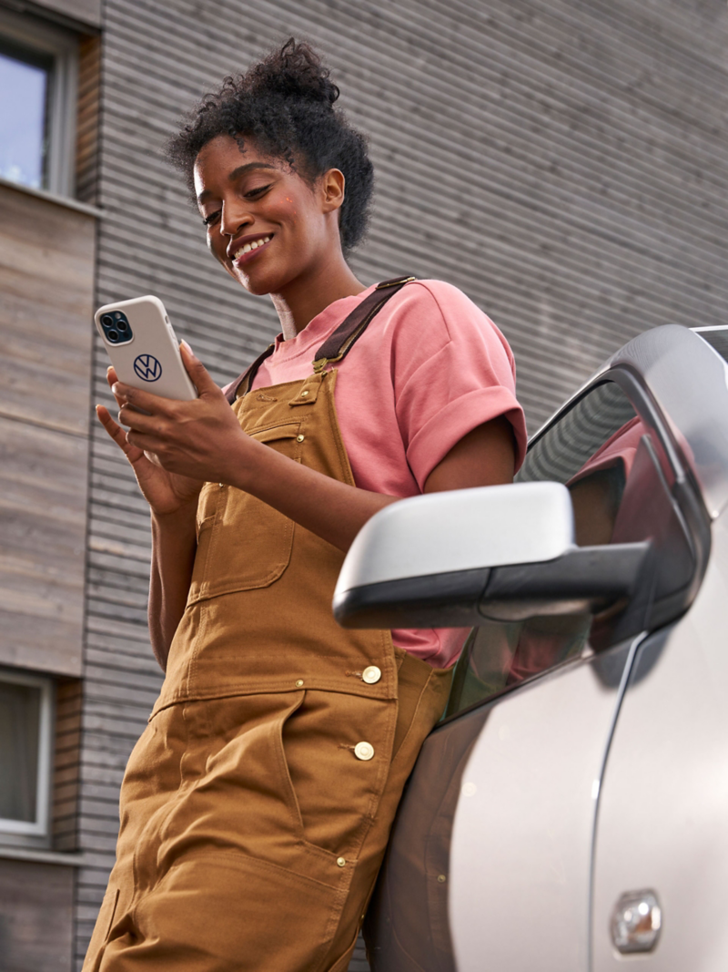 Femme appuyée contre une VW Polo 4 et regardant son smartphone