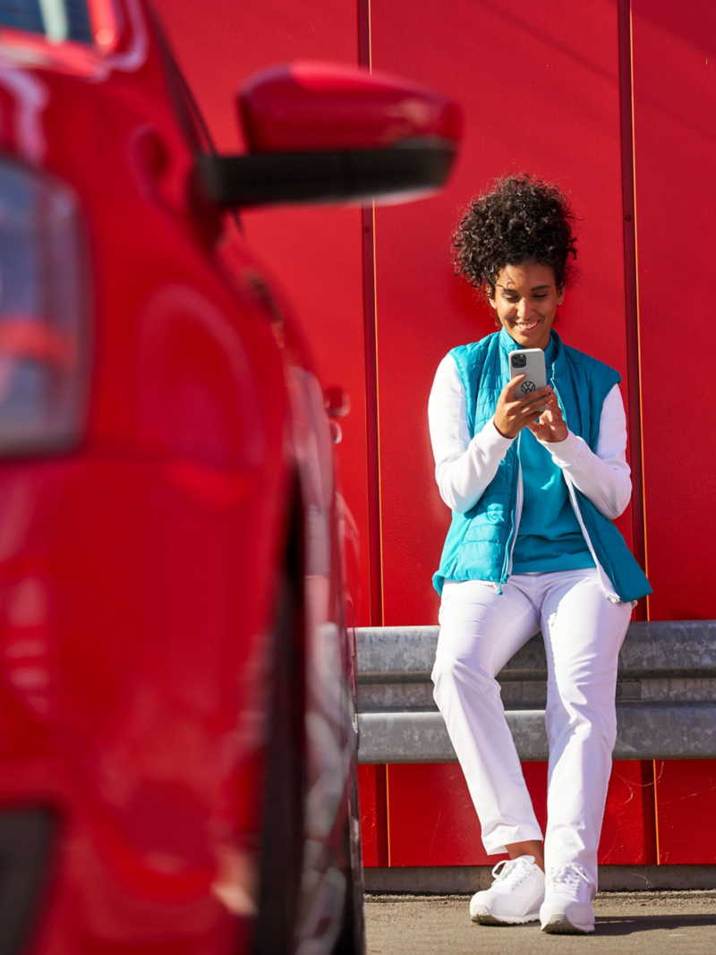 Frau schaut auf Smartphone, im Vordergrund ein roter VW Polo 5