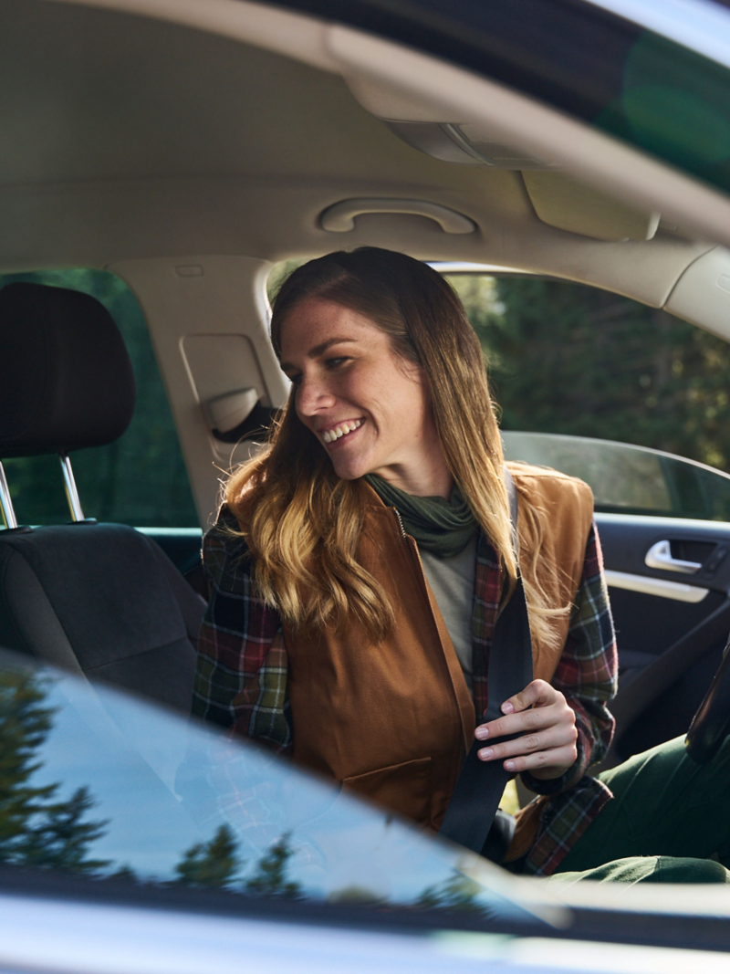 Woman sits in a VW Tiguan 1 and looks backwards while fastening her seatbelt