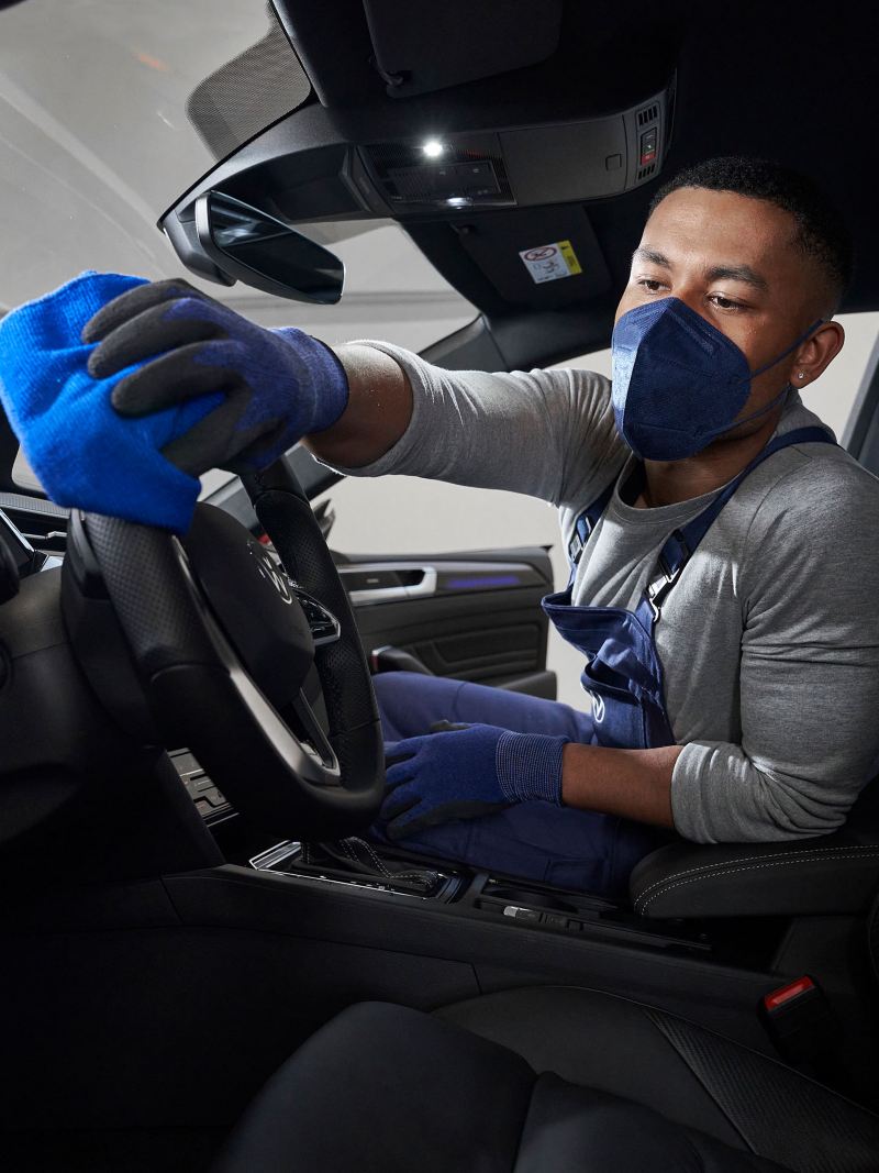 Ein VW Servicemitarbeiter desinfiziert den Innenraum eines Volkswagen – Service in der Corona-Lage