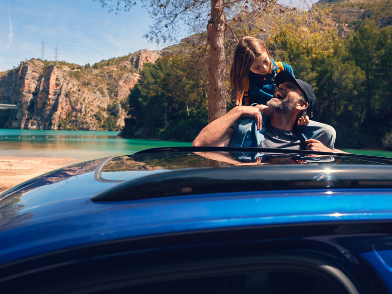 A man gives a child a piggy back, the roof of a VW Touareg R can be seen in the foreground