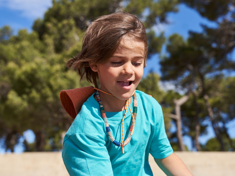 Kind mit Hut und Halskette spielt im Sand