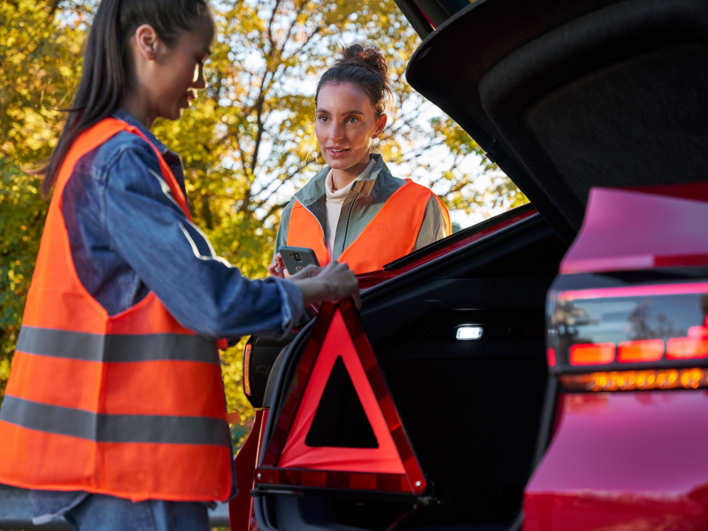 Two women with safety vests and warning triangle next to VW ID.5 GTX