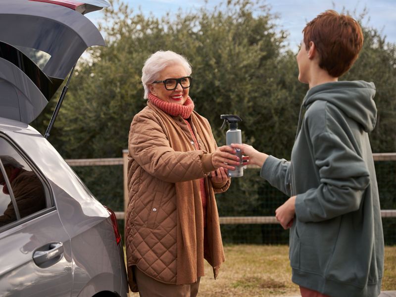 Vrouw geeft een andere vrouw een fles onderhoudsproduct van VW-accessoires