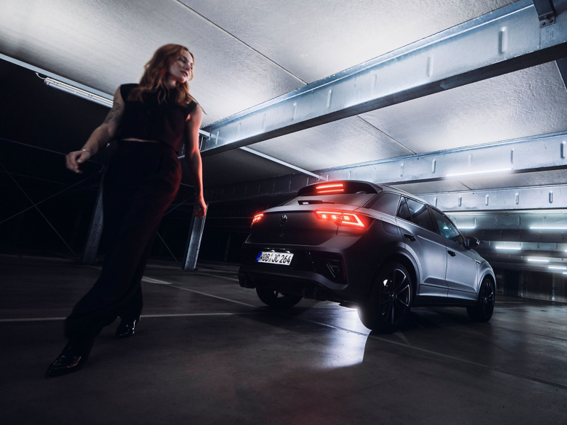 Rear view of VW T-Roc R with illuminated brake lights, woman walking in the foreground