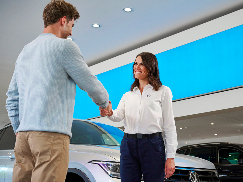 Un uomo stringe la mano ad una venditrice in una concessionaria VW