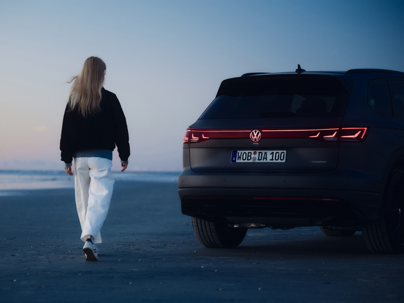 Frau läuft auf Heck eines VW Touareg R FINAL EDITION mit leuchtender Lichtsignatur zu
