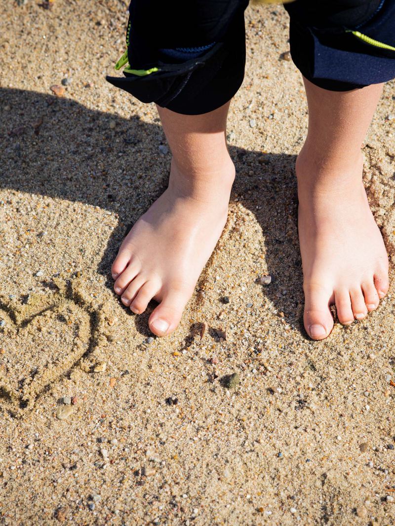 Nahaufnahme von Füßen im Sand neben einem in den Sand gezeichneten Herz
