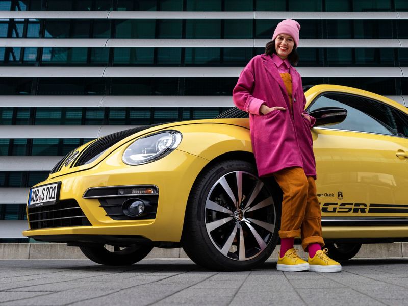 Kobieta oparta o swojego Volkswagena Beetle GSR – starszy model samochodu kompaktowego