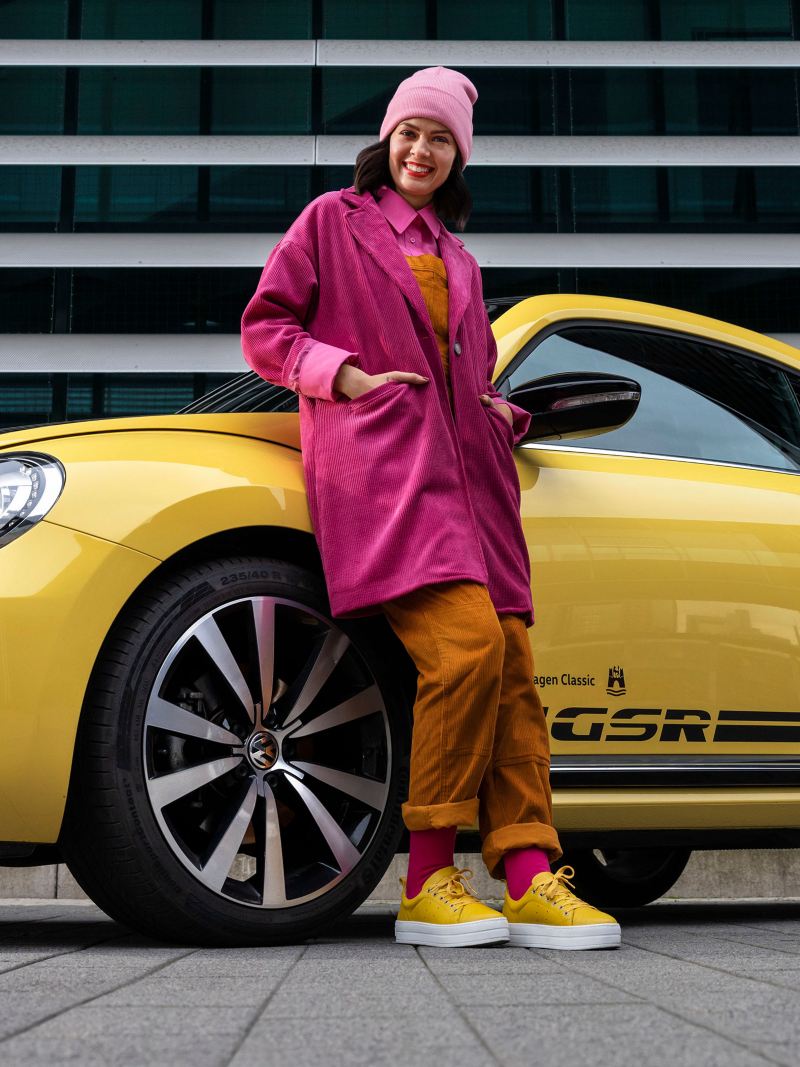 Kobieta oparta o swojego Volkswagena Beetle GSR – starszy model samochodu kompaktowego