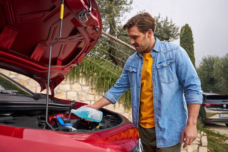 Un uomo davanti al cofano aperto rabbocca il liquido tergicristalli Volkswagen concentrato