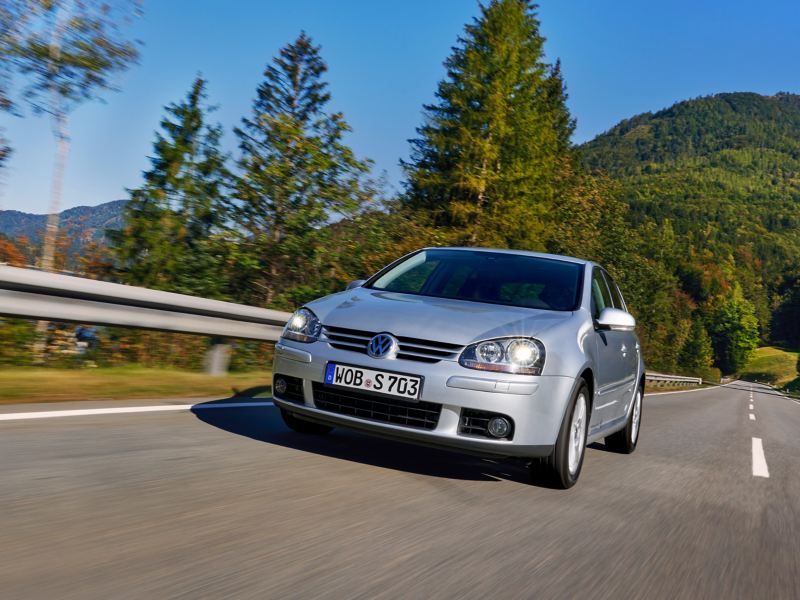 VW Golf 5 driving on a country road, green mountains in the background