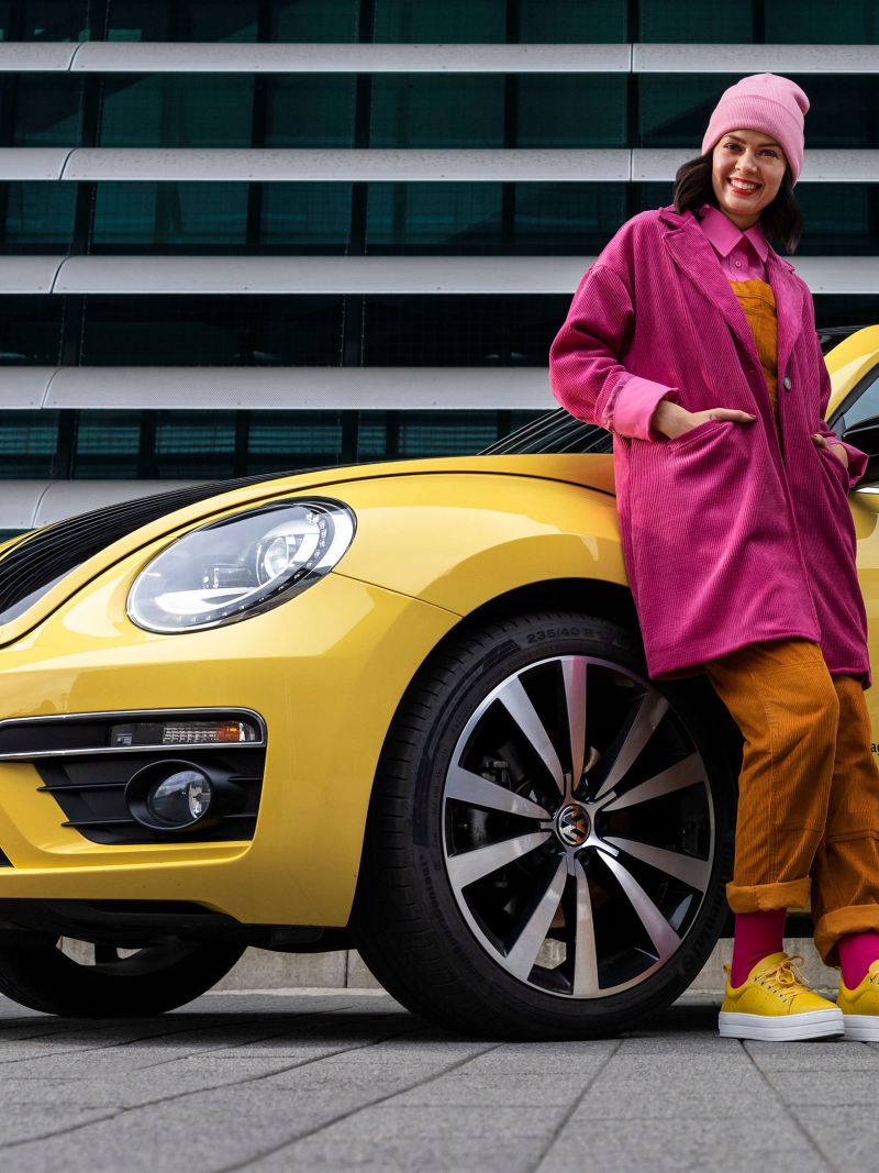 Eine Frau lehnt sich an ihren VW Beetle GSR – Kompaktklasse Vorgängermodell