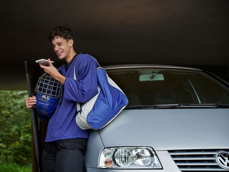 Mann mit Smartphone in der Hand lehnt an seinem VW MPV Modell