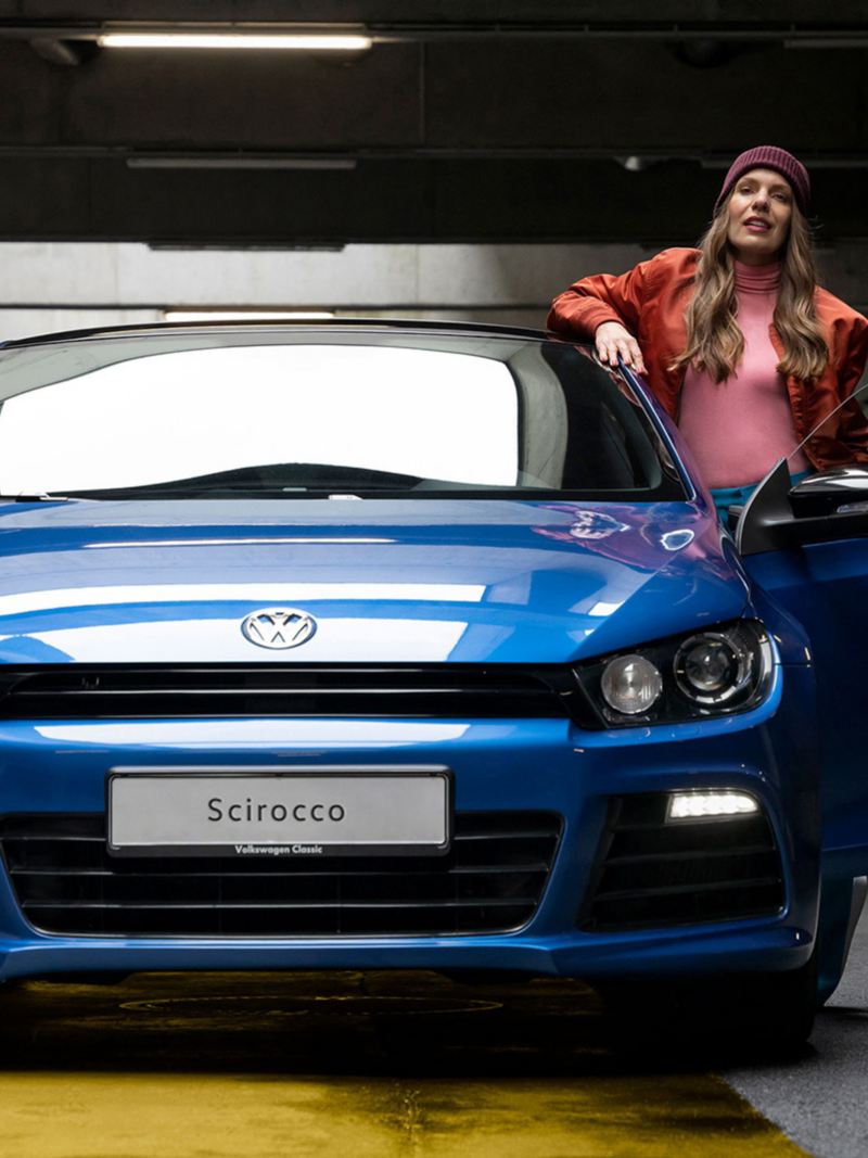 A woman stands next to the open driver's door of the VW Scirocco 3 R