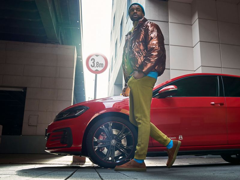 A stylishly dressed man in front of a red VW Golf