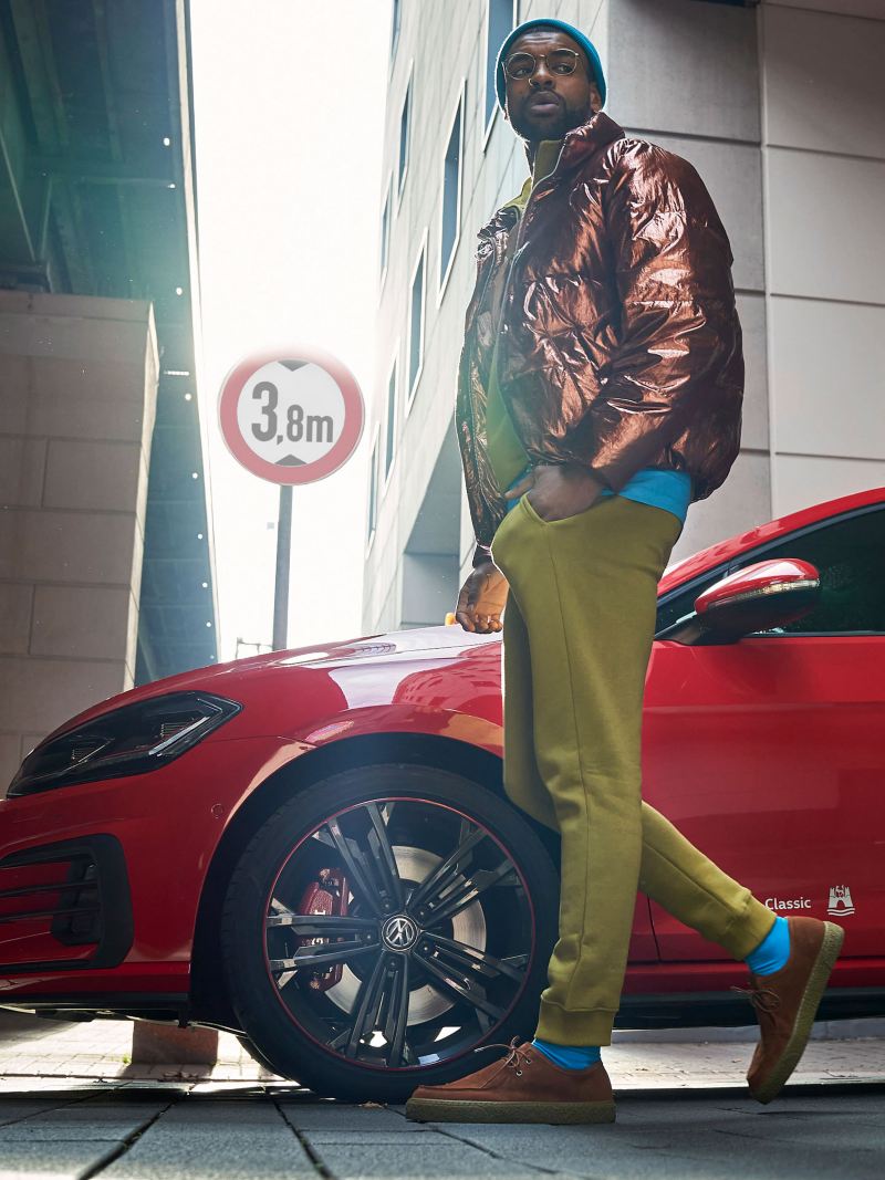 A stylishly dressed man in front of a red VW Golf